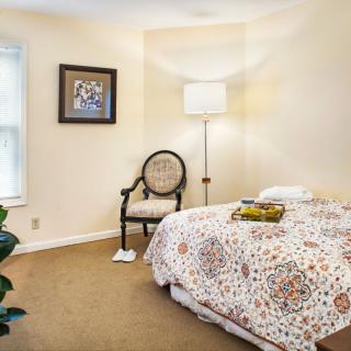 A cozy bedroom with a decorative bedspread, an armchair, a floor lamp, and wall artwork.