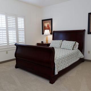 A well-furnished bedroom with a wooden sleigh bed, bedside lamp, and artwork on the walls.