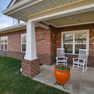 A cozy brick porch with two white rocking chairs and an orange planter.