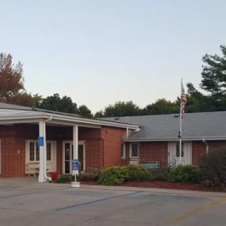 A brick building with a covered entrance and a flagpole, surrounded by trees and parking spaces.