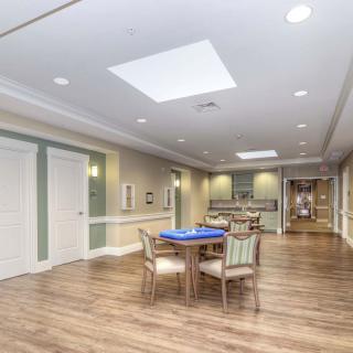 A spacious indoor lounge area with a table and chairs, featuring hardwood flooring and ceiling lights.