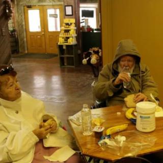 Two people are sitting at a table in a community setting, enjoying a meal together.