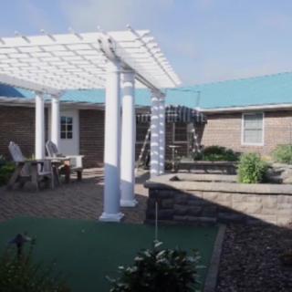 A peaceful outdoor patio area with a pergola, surrounded by landscaping and brick buildings.