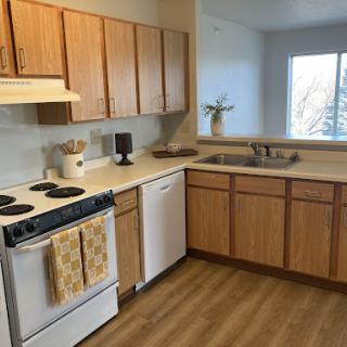 A modern kitchen featuring wooden cabinets and essential appliances, illuminated by natural light.