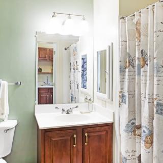 A clean and well-lit bathroom featuring a vanity with a mirror, a toilet, and a shower with a decorative curtain.