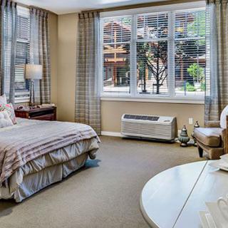 A cozy bedroom interior with a neatly made bed, large window, and soft lighting.