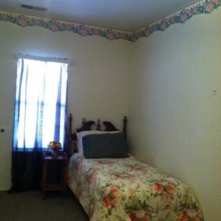 A cozy bedroom with floral bedding, a nightstand, and a window letting in natural light.