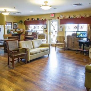 A cozy living room with comfortable seating and a warm wooden floor, decorated with various items and ample lighting.