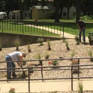 Two people are gardening in a landscaped outdoor area, planting new plants.