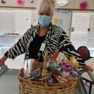 A woman wearing a zebra print jacket and a mask proudly holds a large basket filled with various gifts.