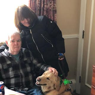 A person enjoying the company of a golden retriever, accompanied by another individual in a cozy indoor setting.