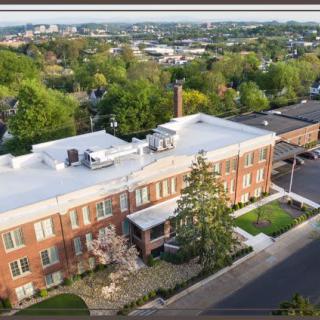 Aerial view of a brick building surrounded by greenery in an urban area.