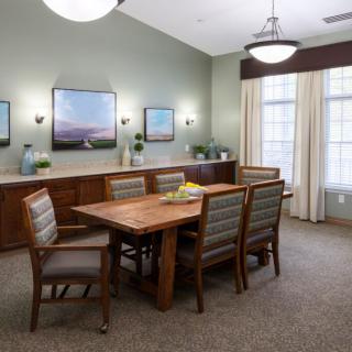 A cozy dining room with a wooden table and six chairs, adorned with paintings and elegant lighting.
