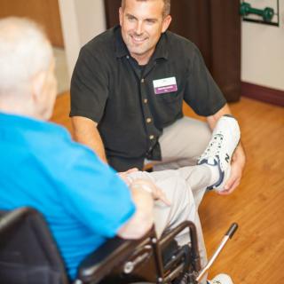 A healthcare professional assists a senior patient in a wheelchair with physical therapy exercises.
