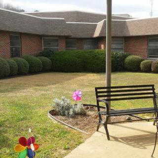 A peaceful courtyard featuring a bench and colorful flowers, surrounded by manicured greenery.