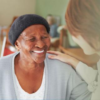 An elderly woman shares a warm smile with a caregiver, highlighting the supportive and caring environment.