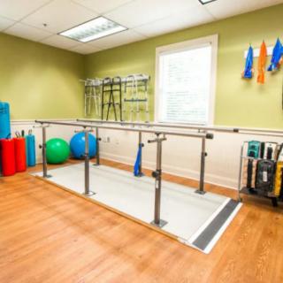 A well-equipped physical therapy room with parallel bars and various exercise equipment.