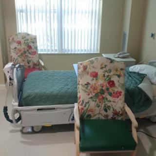A patient room featuring a hospital bed and two floral-patterned chairs.