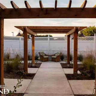 A serene garden pathway featuring a wooden pergola and cozy outdoor seating.