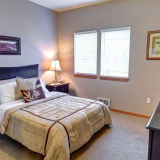 A cozy bedroom with a neatly made bed, nightstand, lamp, and wall art.