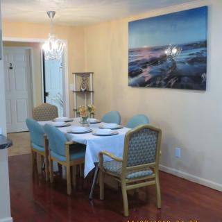 A neatly set dining table with a white tablecloth and light blue chairs, situated in a warmly lit room adorned with artwork on the wall.