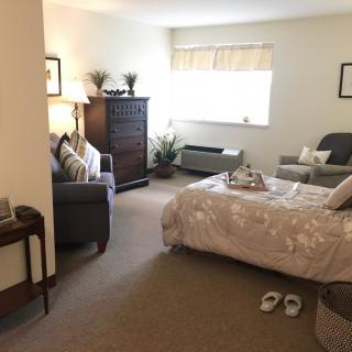 A cozy bedroom with a neatly made bed, armchair, and dresser.