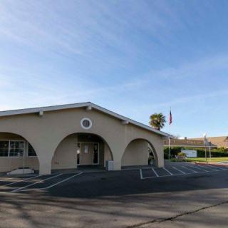 A building with arched entrances and a parking lot in front, featuring a flagpole under a clear sky.