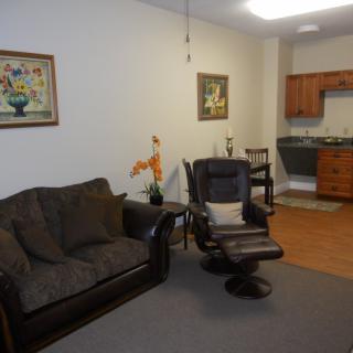 A cozy living room with a sofa, armchair, and an adjoining kitchen area.