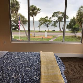 A cozy bedroom with a picturesque view of a lake and palm trees through the window.