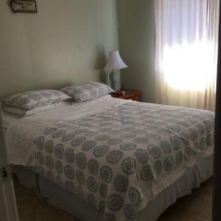A cozy bedroom with a neatly made bed, bedside lamp, and sheer curtains letting in light.