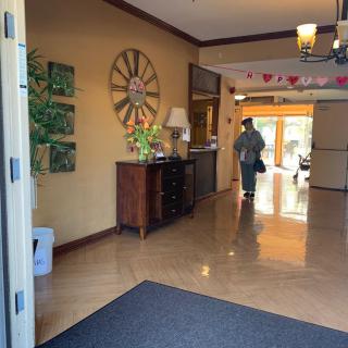 A warmly decorated entrance hall with a large clock and wooden furniture, featuring a person walking through the hallway.
