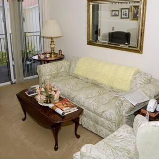 A cozy living room featuring a patterned sofa, a wooden coffee table adorned with books and decorations, a large mirror on the wall, and plush carpet flooring.