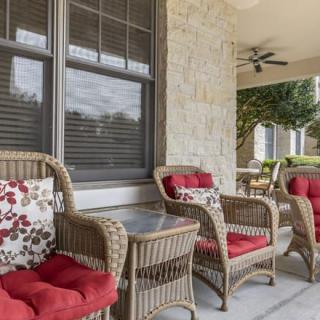 A cozy porch with wicker furniture adorned with red and floral cushions, set against a stone wall.