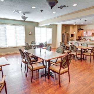 A brightly lit dining area with tables and chairs, adjacent to a kitchen.