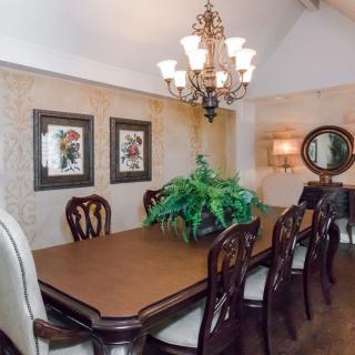Elegant dining room with a wooden table, upholstered chairs, a central chandelier, and decorative wall elements.