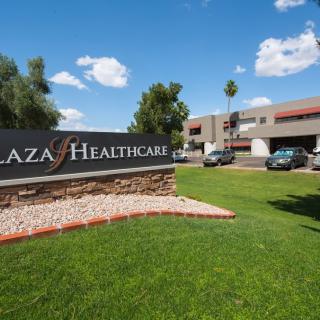A healthcare facility with a prominent sign, surrounded by green grass and trees under a blue sky with clouds.