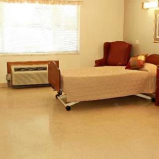 A simple hospital room with a single bed and an armchair next to a window.