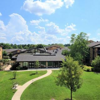 A residential building surrounded by a lush green lawn and trees under a partly cloudy sky.