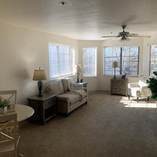 A spacious living room filled with natural light, featuring a sofa, lamps, and several large windows.