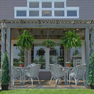 A cozy outdoor patio with wicker furniture and lush greenery under a pergola.