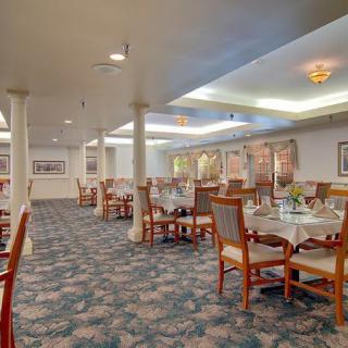 A spacious dining area featuring neatly arranged tables and chairs, with soft lighting and patterned carpeting.