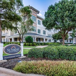 A view of a residential building surrounded by well-maintained landscaping and trees, with a sign in front.