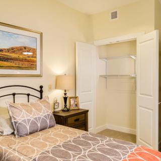 A cozy bedroom featuring a neatly made bed, a decorative lamp, and an open closet.