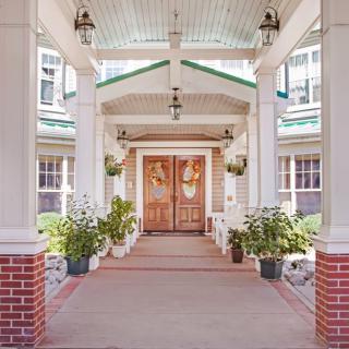 A welcoming entrance with wooden double doors, flanked by columns and decorated with hanging lanterns and potted plants.