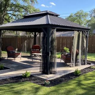 A charming gazebo with patio furniture, set in a neatly landscaped backyard on a sunny day.