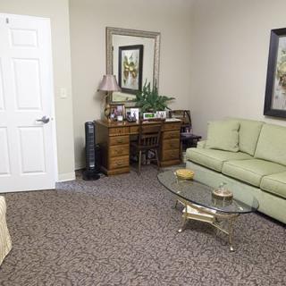 A cozy living room with a green sofa, glass coffee table, and wooden dresser.
