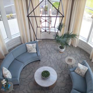 A stylish living room featuring curved sofas, a central coffee table with plants, and large windows allowing natural light.