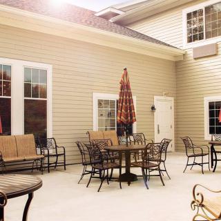 A sunny outdoor patio area with tables, chairs, and an umbrella set against a building exterior.
