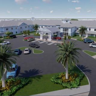 Aerial view of a large building with a circular driveway and parking area surrounded by palm trees.