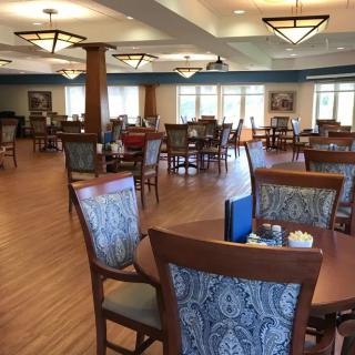 A spacious dining room with multiple tables and chairs, featuring large windows and elegant lighting.